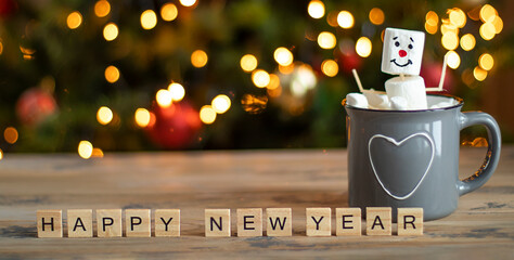A marshmallow man sits in a mug of cocoa on the background of a Christmas tree. Happy New Year