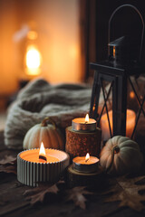 Cozy autumn composition with aromatic candle, pumpkins, wool sweater, leaves, cinnamon. Aromatherapy on a grey fall morning, home atmosphere of cosiness and relax. Wooden background close up.