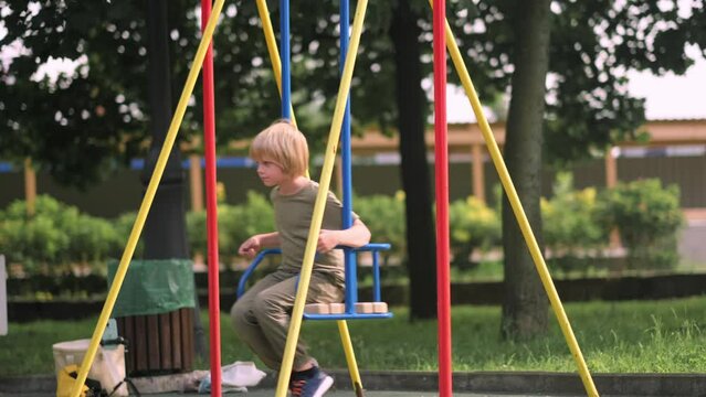 Boy swinging on swing in park, child having fun , playing on outdoor public playground, kids play on school or kindergarten yard, active kid on colorful swing, healthy summer activity for children