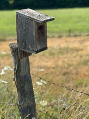 wooden bird house on a fence post in the countryside on a summer day