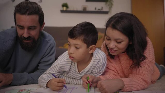 Close up young multiracial parents helping only child with homework at home. United family doing creative activities lying in living room. Concept of home schooling and childhood development.