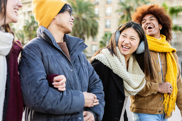 Young group of diverse happy friends having fun enjoying winter vacation together in city street.