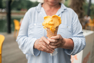 Happy smiling senior woman dressed in stylish clothes eating ice cream in the city summer outdoors...