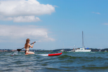 Young woman riding stand up paddle board in the sea. Healthy and fit life in the nature.