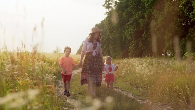 A magical video of a mother walking along a country road holding her children by the arms. The concept of family happiness, freedom and peace, children and parents mutual understanding 