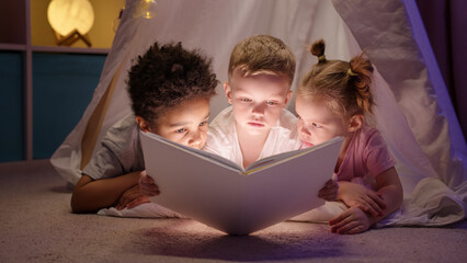 Multi ethnic kids caucasian girl boy afroamerican boy read book lying in wigwam.