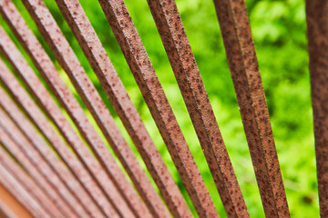 Rusting red and dark brown metal bars in fan formation with blurry green background asset