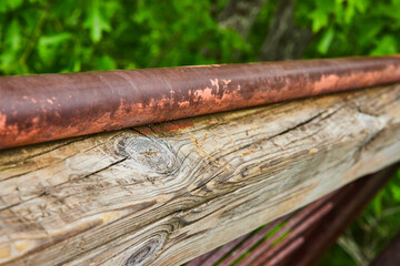 Fading and chipped red paint on metal pole resting on carved wood beam with cracks and wood knots
