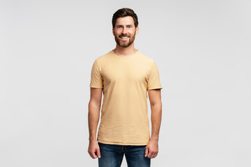 Portrait of smiling handsome bearded man, hipster wearing blank t shirt looking at camera isolated on gray background. Happy successful fashion model posing for pictures, studio shot. Mockup