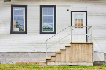 Common whit house with white door and concrete steps and items crowding windows exterior