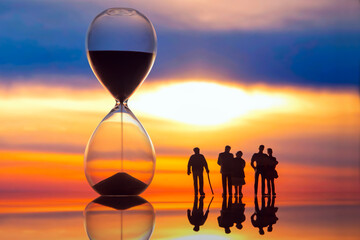 miniature people. silhouettes of different people watching the sunset next to the hourglass. end of...