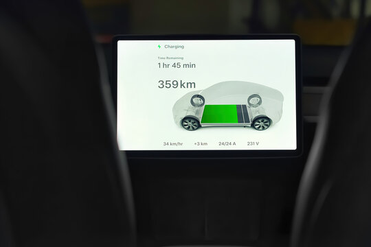 Toronto, Ontario, Canada - July 16, 2023 :  Close up of Tesla control panel touchpad screen showing battery charging progress and time remaining information. Green energy and electric car background. 