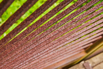 Macro red and dark brown metal spokes or square bars over blurry tree top trail background asset