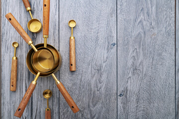 Copper measuring cups with wooden handles on gray kitchen table. View from above. Space for text.