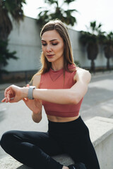 Young sporty woman checking at smartwatch during training and running in the city. Girl athlete fixes the results of her morning online workout.