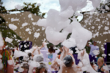 Foam party, children have fun, raising their hands up, catching soap bubbles in the water park. Foam party on the beach for children and adults. Children have fun in soapy foam in summer