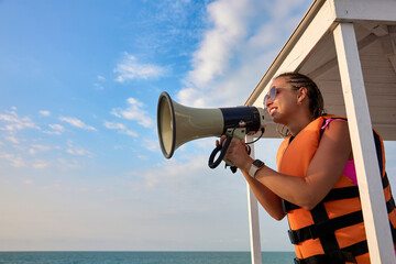 Young woman against the blue sky stands in a rescue tower in a protective vest transmits the...