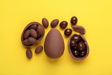 Delicious chocolate eggs and sweets on yellow background, flat lay