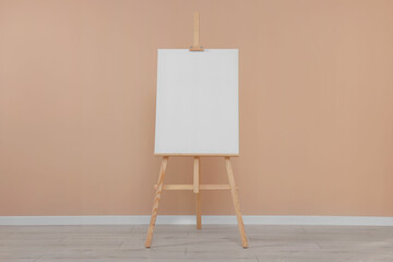 Wooden easel with blank canvas near beige wall indoors.