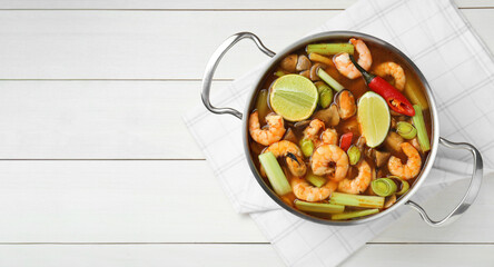 Saucepan with delicious Tom Yum soup on white wooden table, top view. Space for text