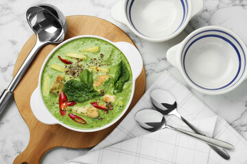 Saucepan with delicious green curry chicken soup and kitchenware on white marble table, flat lay