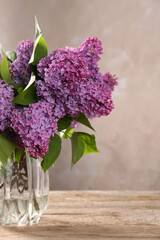 Beautiful lilac flowers in vase on wooden table, space for text
