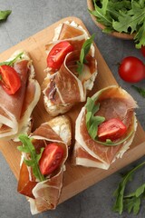 Tasty sandwiches with cured ham, tomatoes and arugula on grey table, flat lay