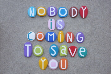 Nobody is coming to save you, creative slogan composed with multi colored stone letters over beach...