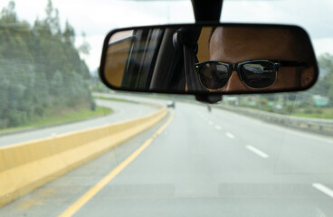 A man driving on the road, looking at the rearview mirror inside the car
