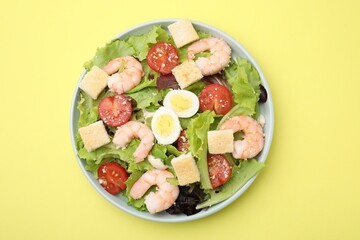 Delicious Caesar salad with shrimps on yellow background, top view