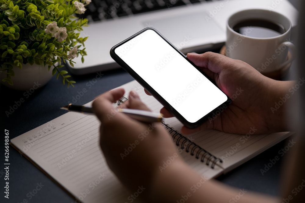 Poster close up view young man sitting at home office desk and using smart phone. blank screen for your tex