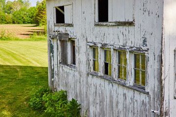 Side of abandoned white country home with chipped paint and busted windows