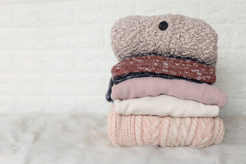 Fall winter season knitwear. Stack of knitted warm pastel color sweaters with different knitting patterns folded in stack on white wooden table, white wall background. Close up, copy space for text