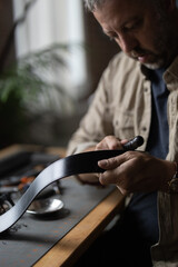 Man doing leatherwork, in a leather working workshop, making a black leather belt
