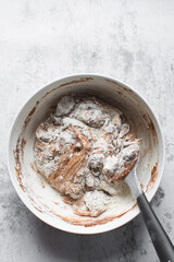 Chocolate cake batter being mixed in a white bowl, folding cake batter in a white mixing bowl, the process of making chocolate cake