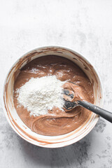 Chocolate cake batter being mixed in a white bowl, folding cake batter in a white mixing bowl, the process of making chocolate cake