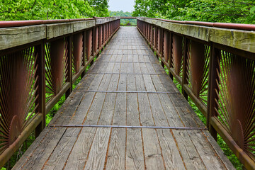Long view of bridge with worn planks and rusty rising sun pattern on railing bars