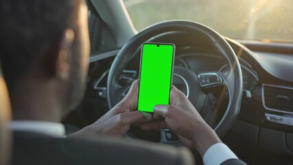 View from back. African American man in suit sitting in car and looking best way to get to office. Young businessman using his smart phone while sitting in car. Concept of driving, technologies, job.