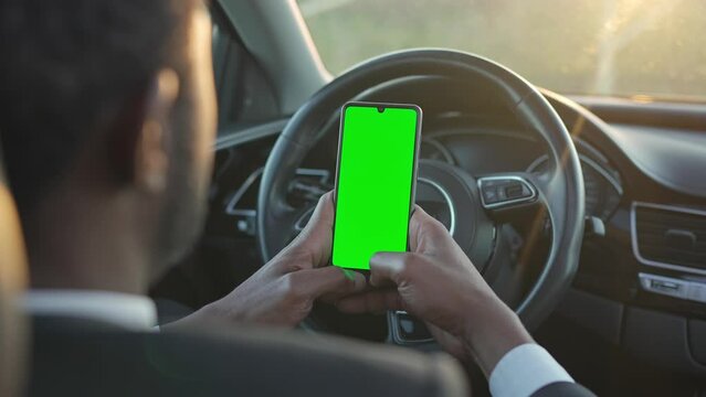 View from back. African American man in suit sitting in car and looking best way to get to office. Young businessman using his smart phone while sitting in car. Concept of driving, technologies, job.