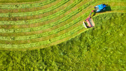 Background asset aerial of blue tractor pulling mower in curved wave line over green field