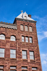 Vertical of old dark brown brick building with fancy roof and half moon above in blue sky
