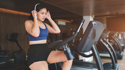 Fototapeta na wymiar Beautiful young woman wearing headphone, doing cardio workout, cycling bikes in gym.