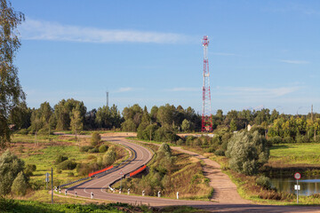 Fototapeta na wymiar Rural landscape in summer. Winding road passing through the bridge. Cell tower on blue sky background.