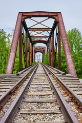 Fototapeta na wymiar Train tracks leading to rusty iron truss railroad bridge leading through trees to city in Ohio