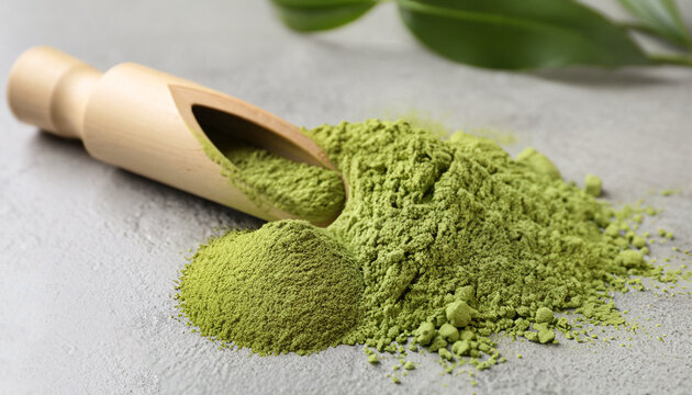 Green matcha powder and bamboo scoop on light grey table, closeup