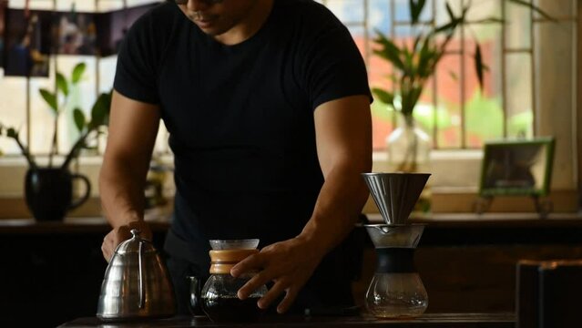 a man wear black only torso and arms drip coffee by pot and jar in morning at home