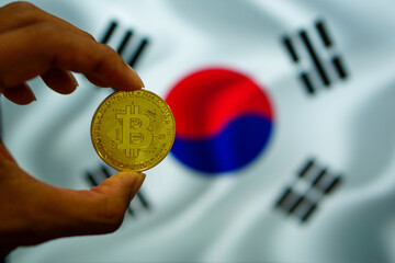 Man's hand with gold bitcoin in hand on South Korean flag background.