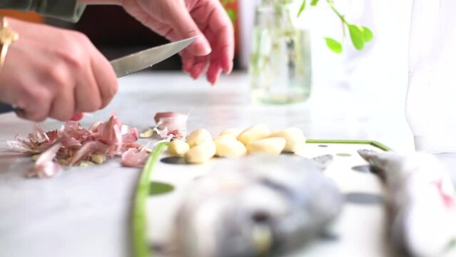 hand peeling garlic next to a sea bream and a whiting on the work surface