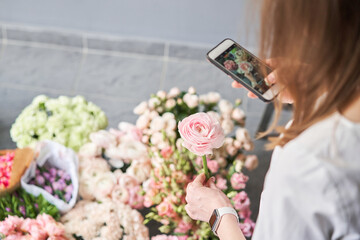 A woman takes a photo on her phone of flowers. Floral shop concept . Florist woman creates flower...