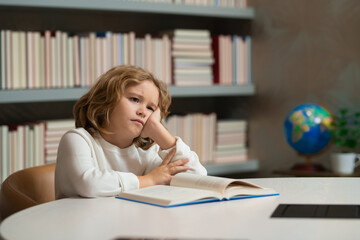 Tired school boy, bored pupil at school. Child pupil reading book in a book store or school library. Kid study read.